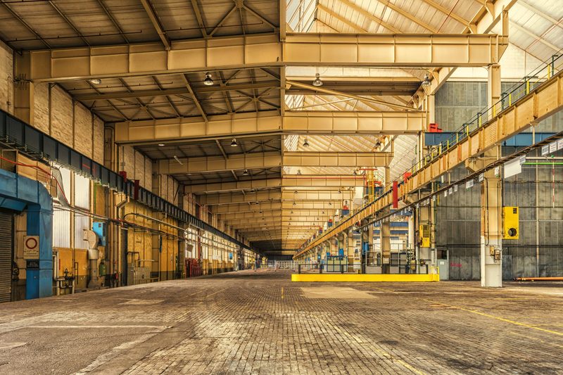 Interior of an industrial warehouse building showing structural steel bays and overhead lighting